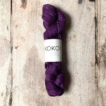 A skein of KOKON Merino Linen Fingering yarn in Byzantium color, placed on a wooden surface.