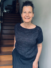 Woman wearing a black and knitted top standing in front of a staircase. The hand knitted top is the knitted by Tash and the name of the pattern is sandhuller